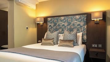 Une chambre d’hôtel avec un grand lit, une tête de lit ornée d’un motif floral, des lampes de chevet et une petite table de nuit.