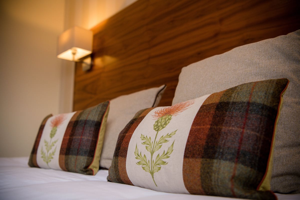 A bed with four pillows featuring plaid patterns and a floral design.