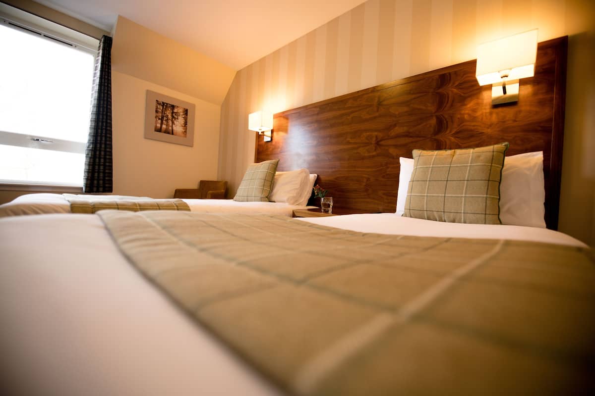 A hotel room with two beds, a wooden headboard, and a window with curtains.