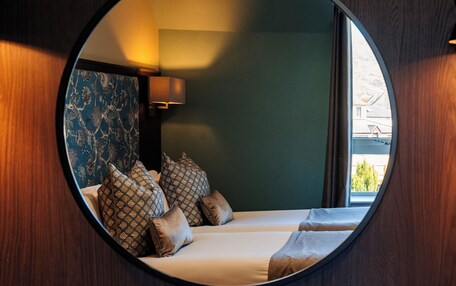 A circular mirror reflecting a room with a bed, pillows, and a nightstand.