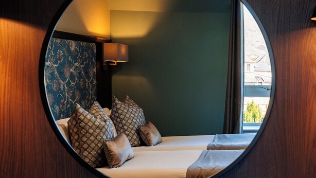 A circular mirror reflecting a room with a bed, pillows, and a nightstand. - Nevis Bank Inn (Fort William)