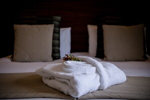 A neatly made bed with a folded white towel and a small decorative branch.