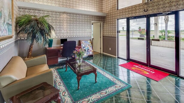 A lobby with patterned wallpaper, a reception desk, a sofa, a coffee table, and a large window with a view of the outside. - Econo Lodge Falfurrias Hwy 281 (Falfurrias)