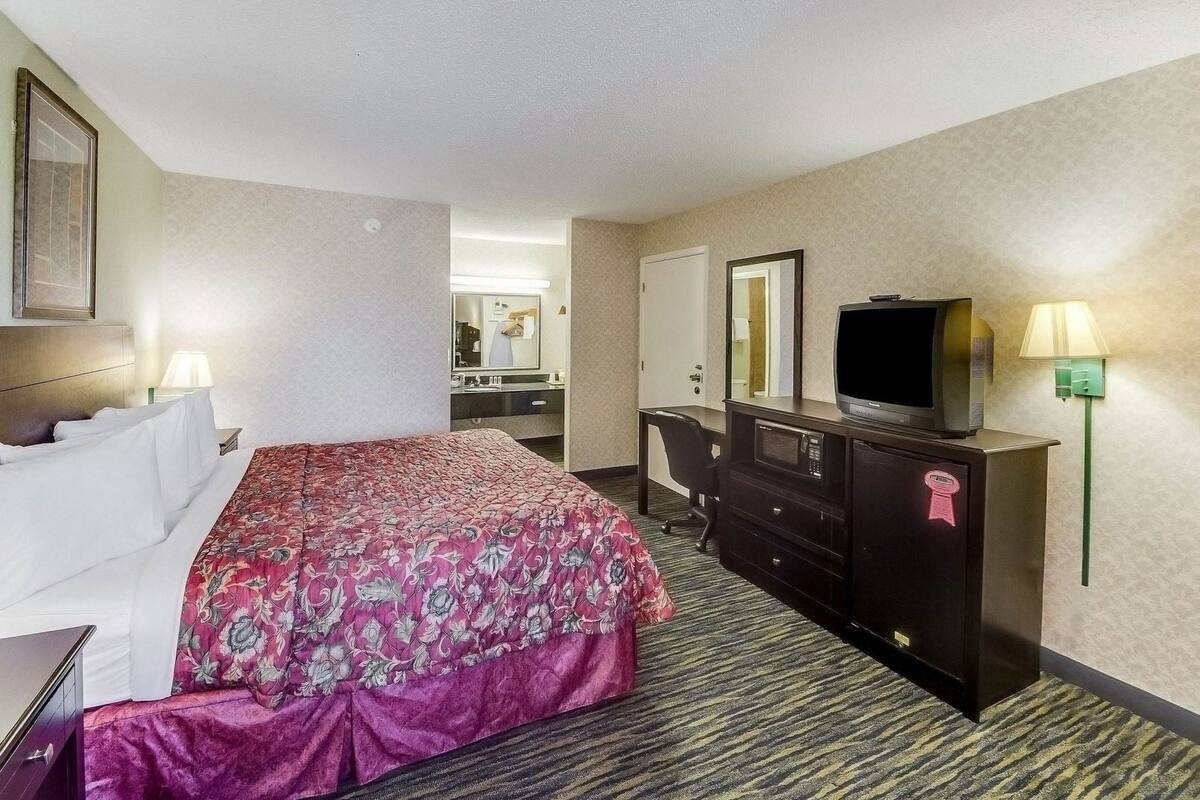 A hotel room with a bed, a desk, a dresser, a television, and a mirror.