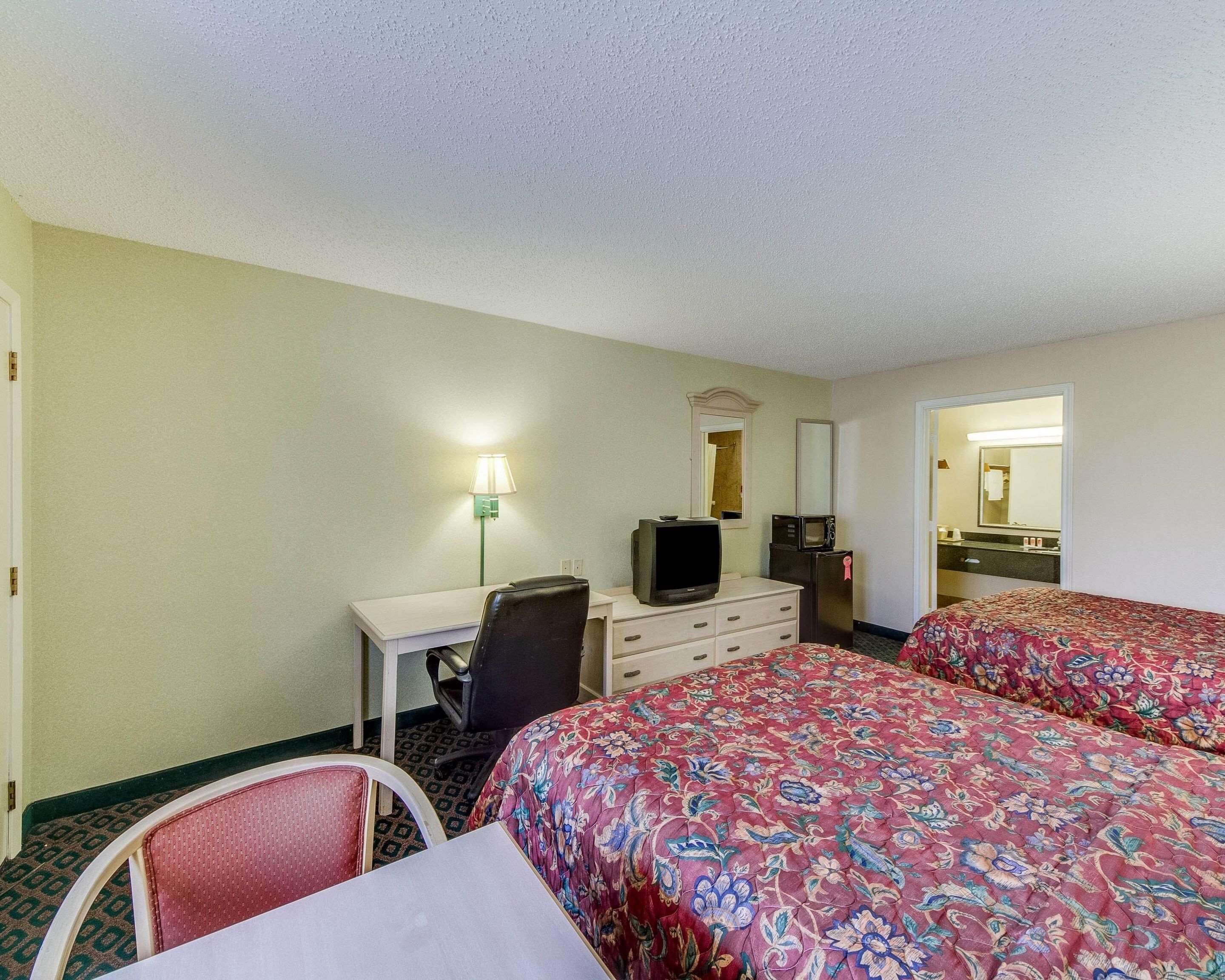 A hotel room with two beds, a desk with a chair, a television, a refrigerator, and a mirror.