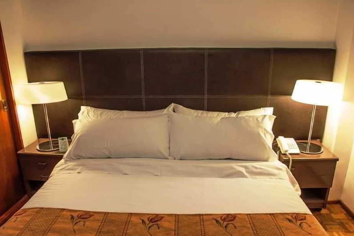 A hotel room with a large bed, two bedside tables with lamps, and a dark headboard.