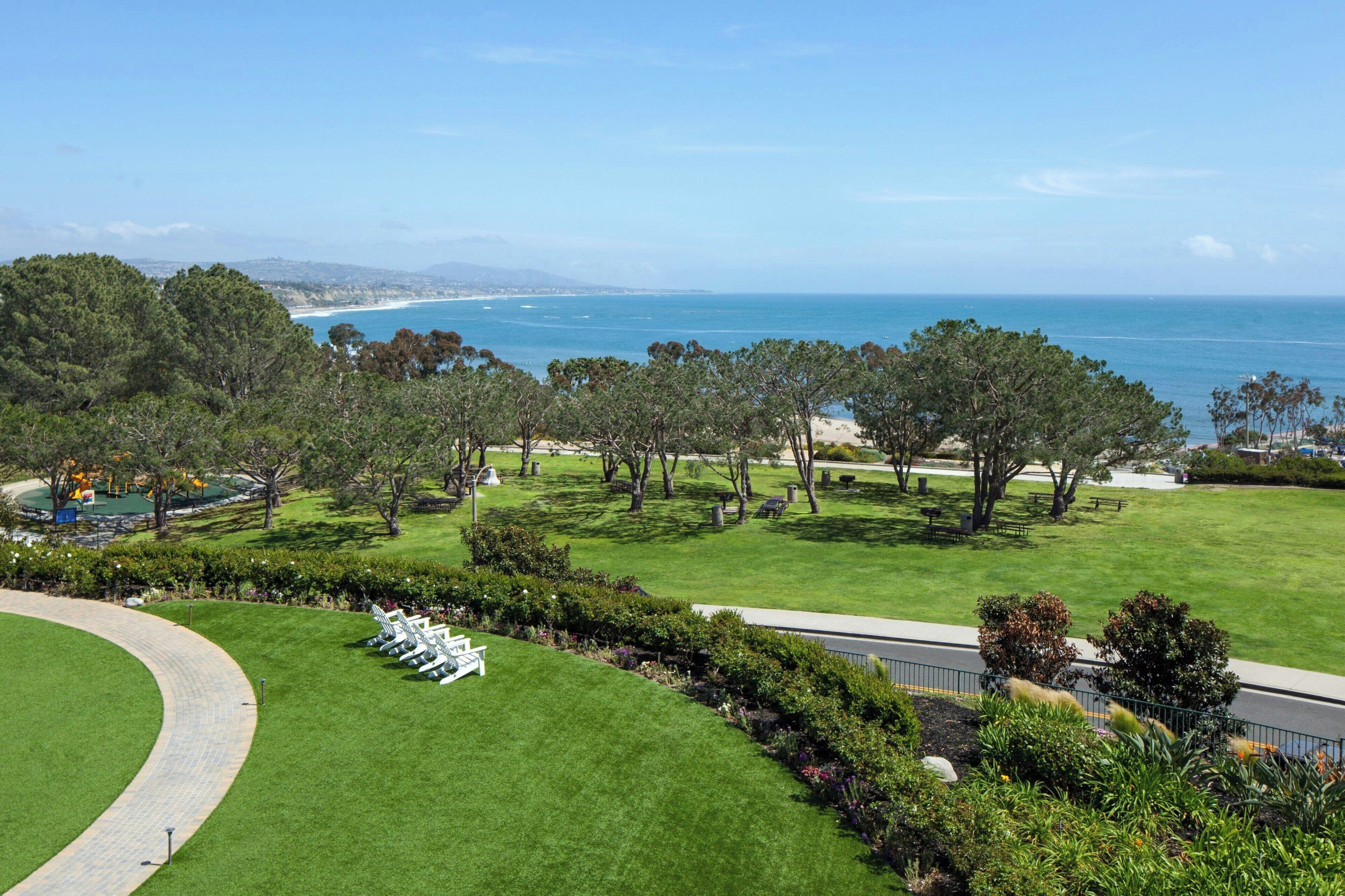 A well-maintained lawn with a curved pathway, a row of white chairs, and a view of the ocean.