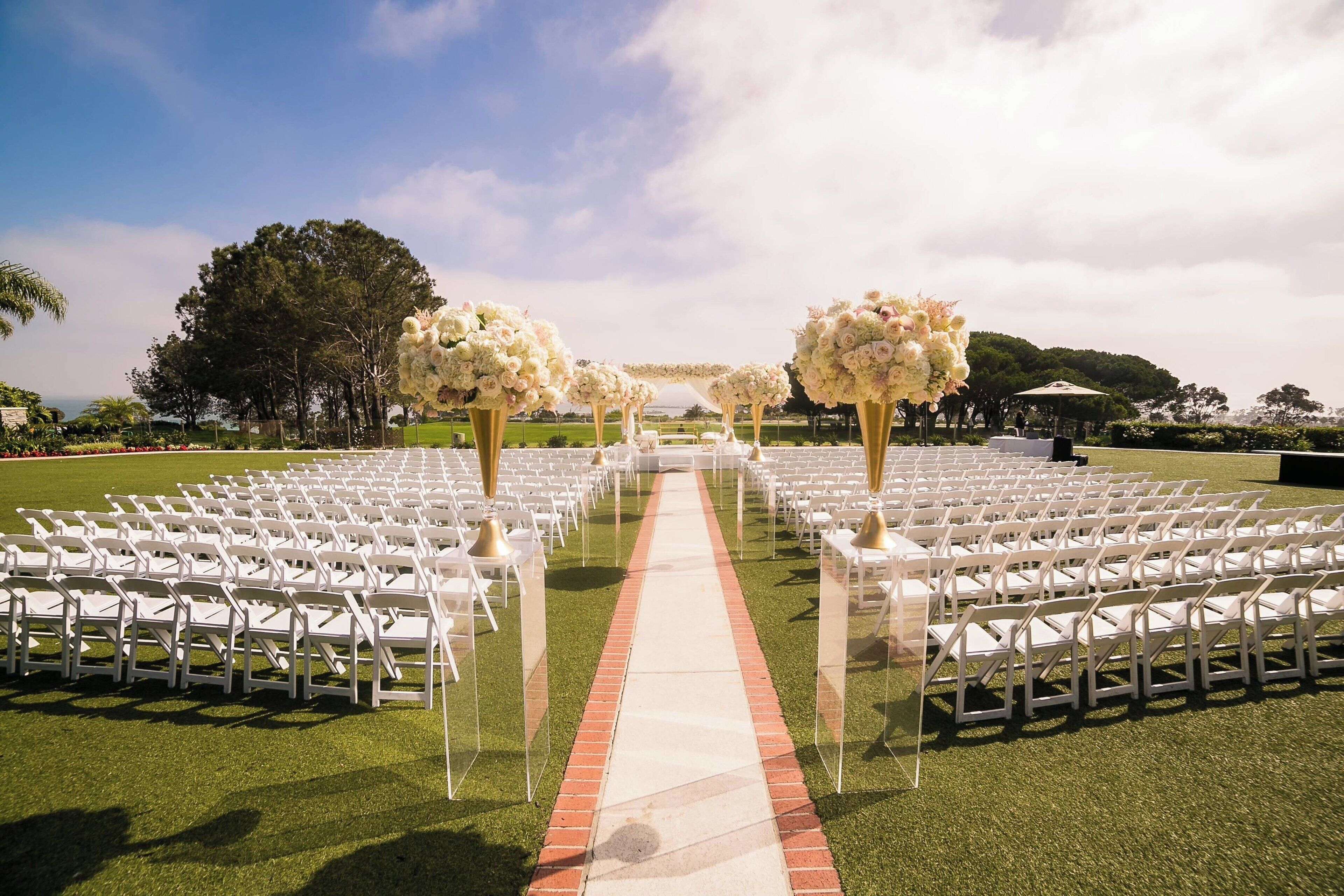 An outdoor wedding venue with rows of white chairs and floral arches.