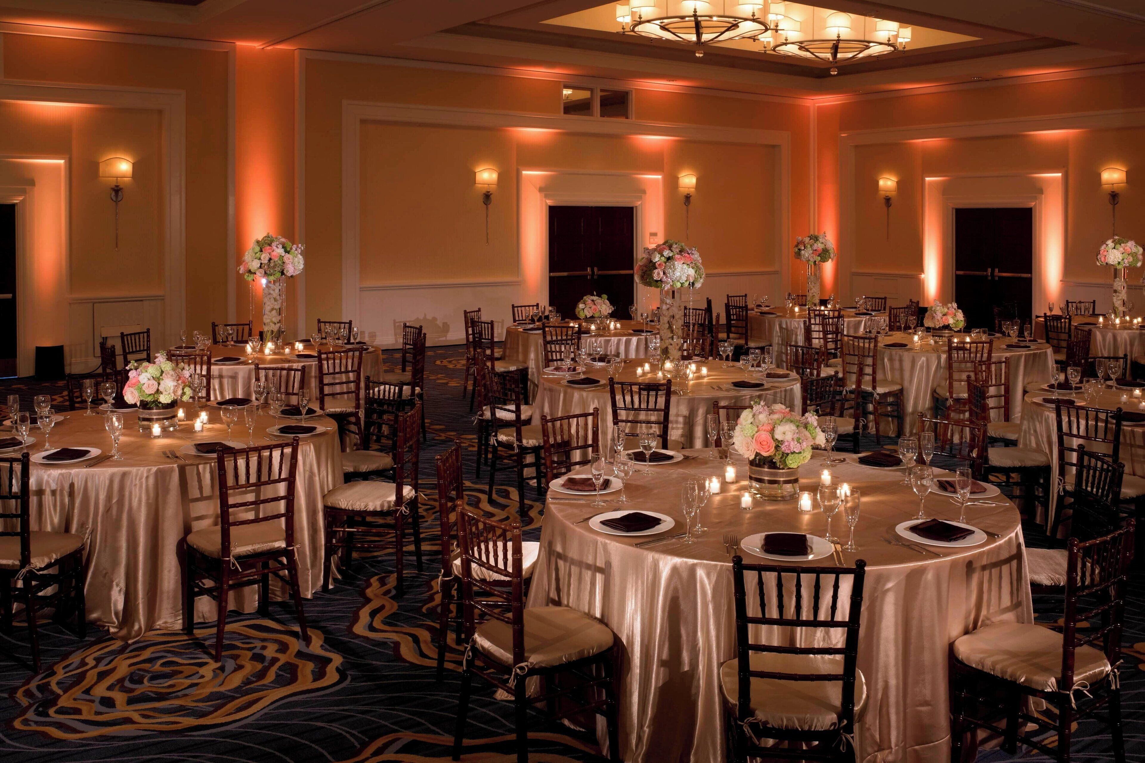 A banquet hall with round tables, chairs, and floral centerpieces.