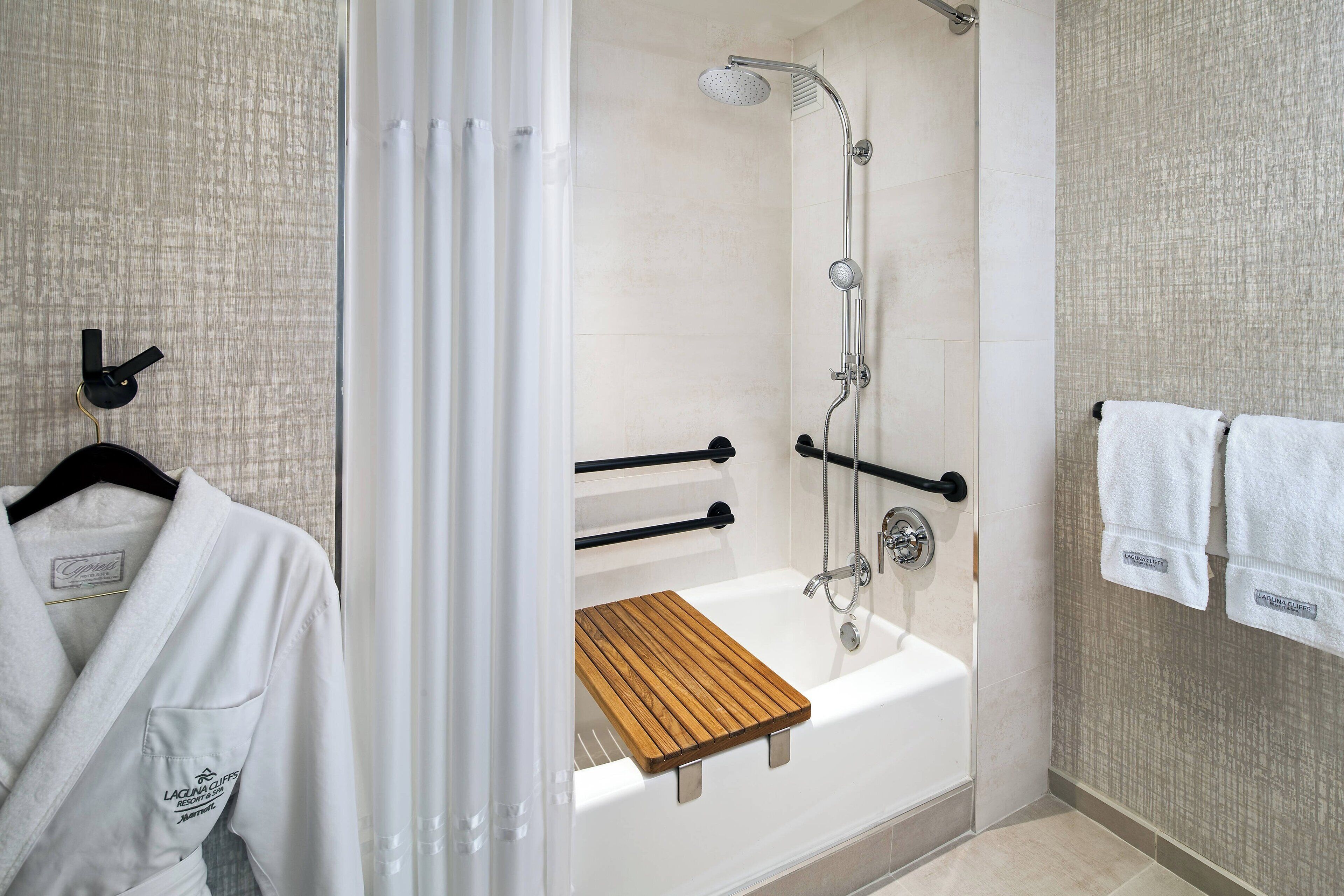 Un baño moderno con cabina de ducha, barras de apoyo y un tapete de baño de madera.