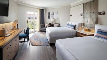 Een hotelkamer met een groot bed, een kleiner bed, een bureau met lamp, een stoel en uitzicht op de omgeving.