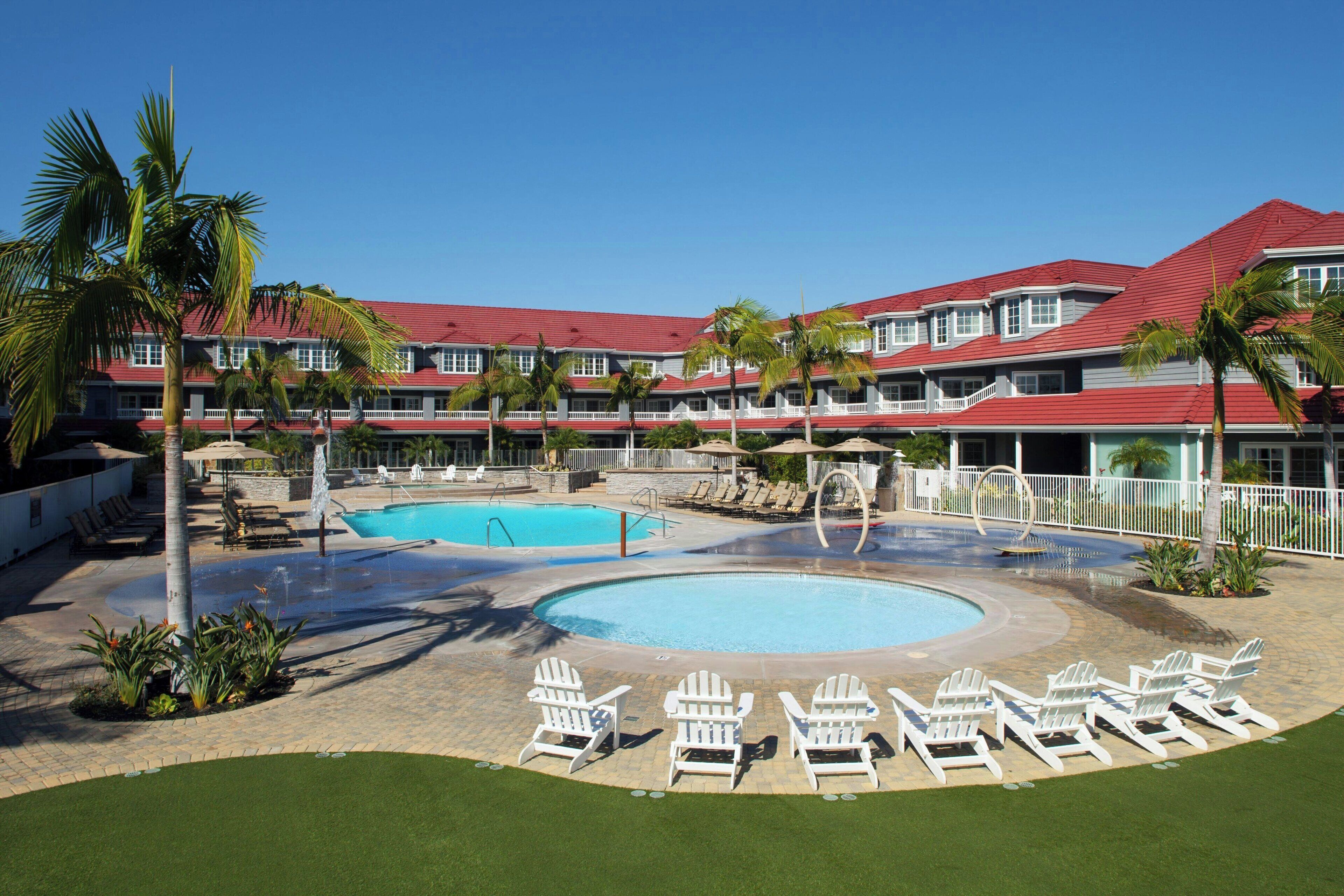 A hotel with a swimming pool, lounge chairs, and palm trees.