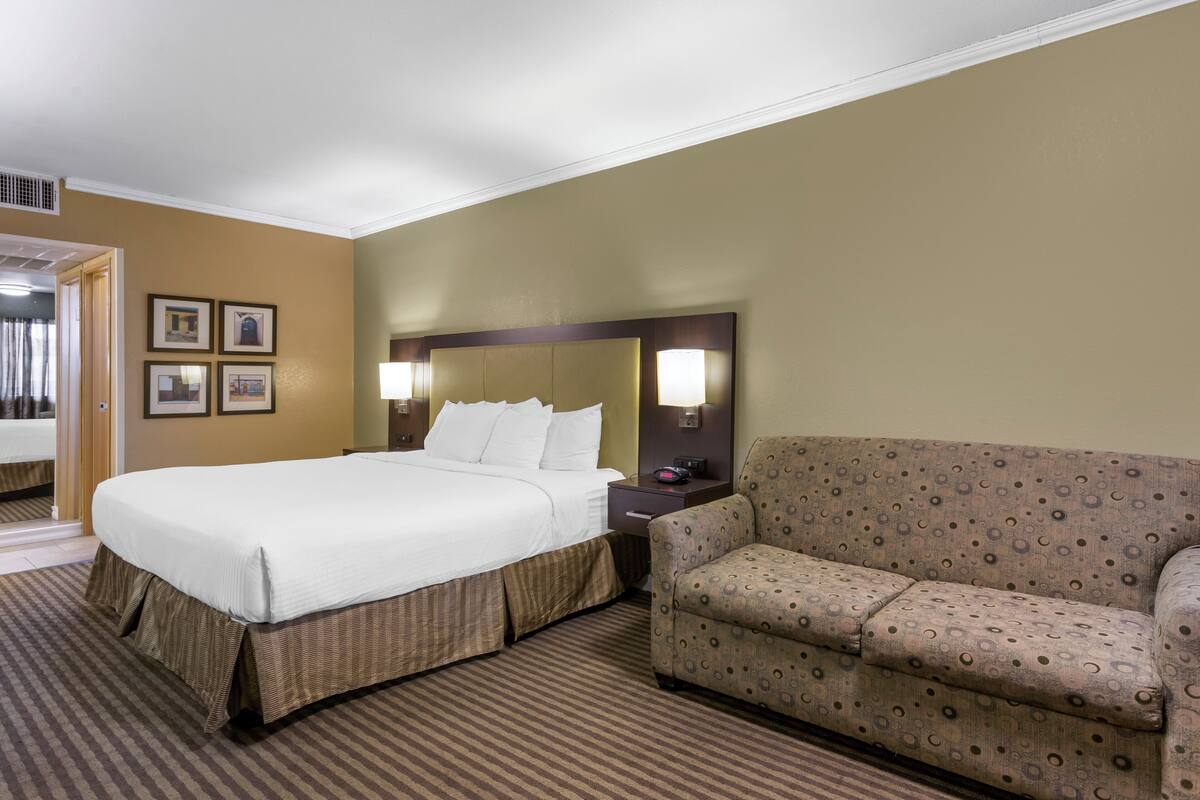 A hotel room with a large bed, a sofa, a nightstand, and a wall with framed pictures.