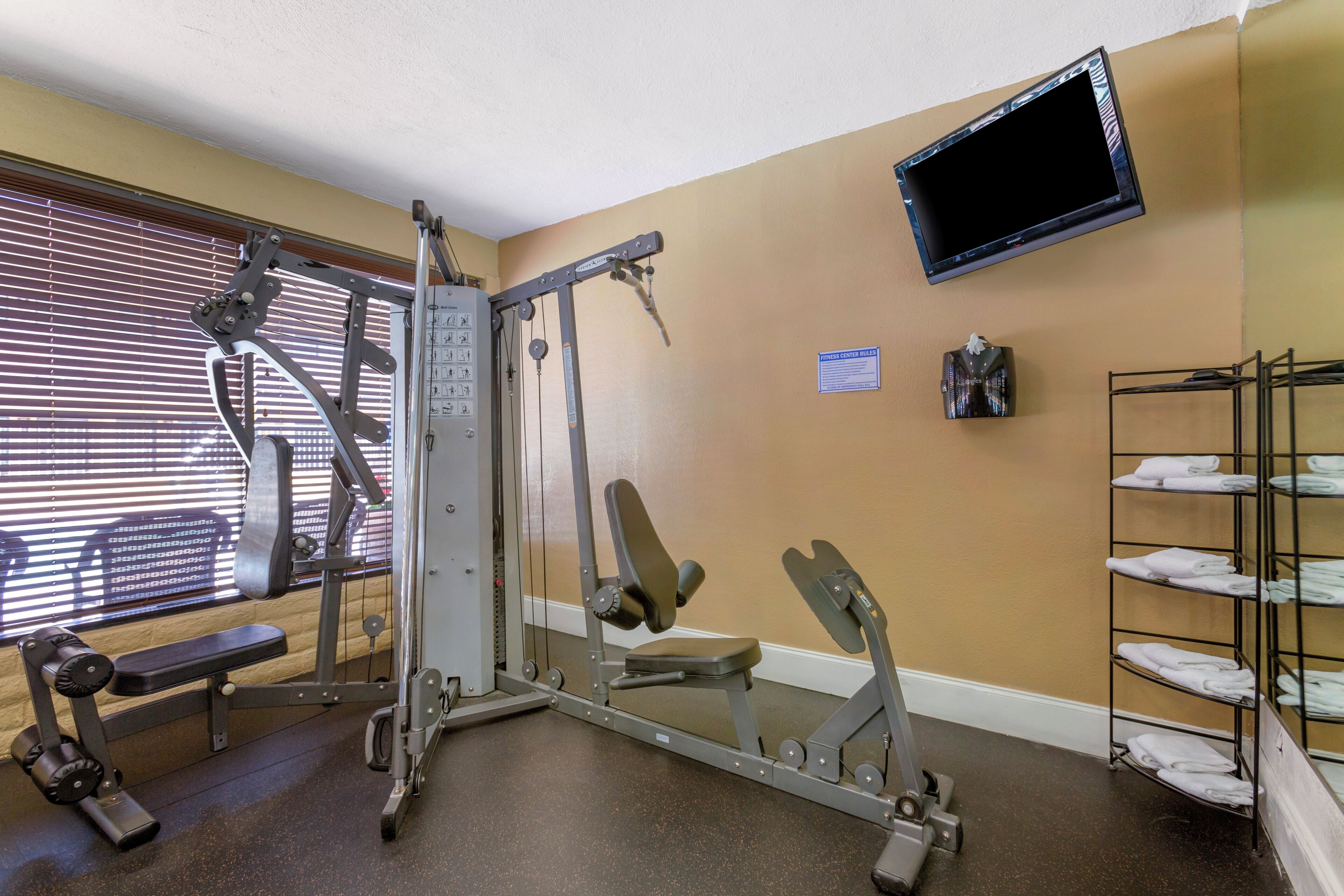 A gym with exercise equipment, a bench, a TV mounted on the wall, and a towel rack.