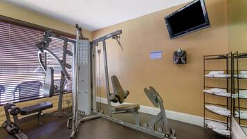 A gym with exercise equipment, a bench, a TV mounted on the wall, and a towel rack.