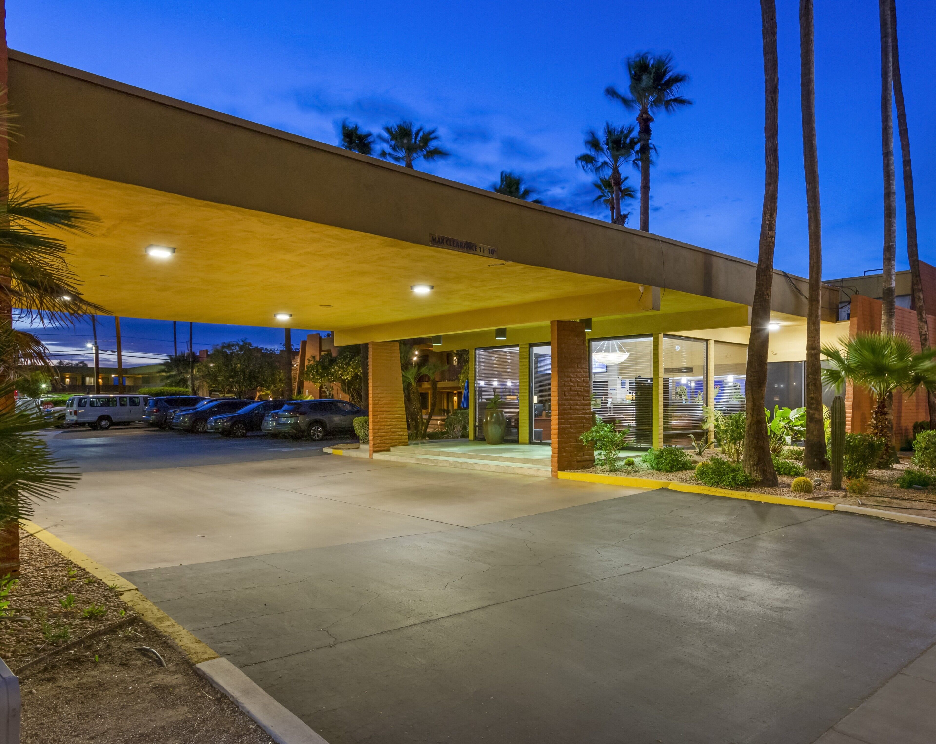A hotel entrance with a covered parking area, palm trees, and a clear sky.