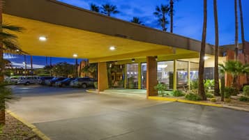A hotel entrance with a covered parking area, palm trees, and a clear sky.