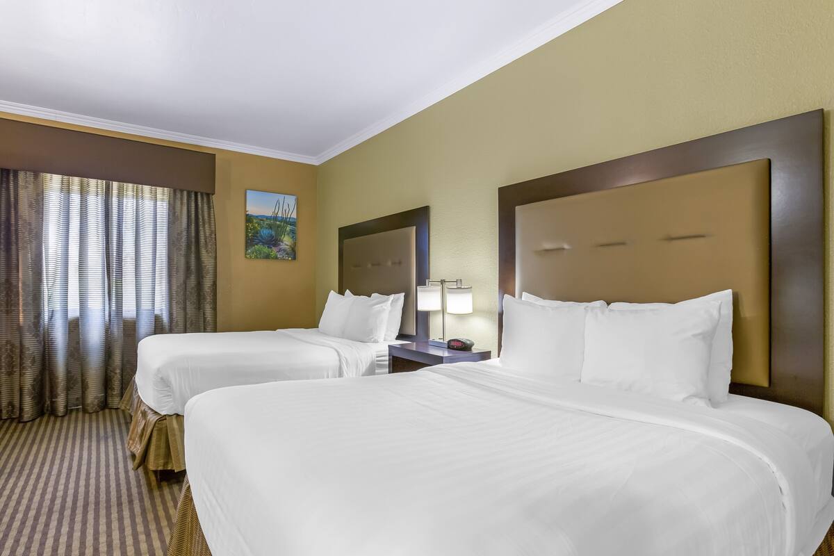 A hotel room with two beds, a painting on the wall, and a window with curtains.