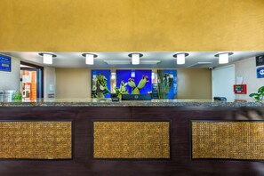 Ein Hotel-Empfangsbereich mit einer Rezeption, einer blauen Wand mit Kakteen-Motiv und einem digitalen Bildschirm.