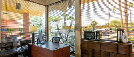 A modern office space with a wooden desk, black office chairs, a computer, and a coffee station.