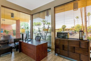 A modern office space with a wooden desk, black office chairs, a computer, and a coffee station. - Royal Sun Hotel & Suites (Tucson)