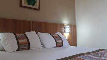 A neatly made bed with white linens and striped pillows, a wooden headboard, and a framed picture on the wall.