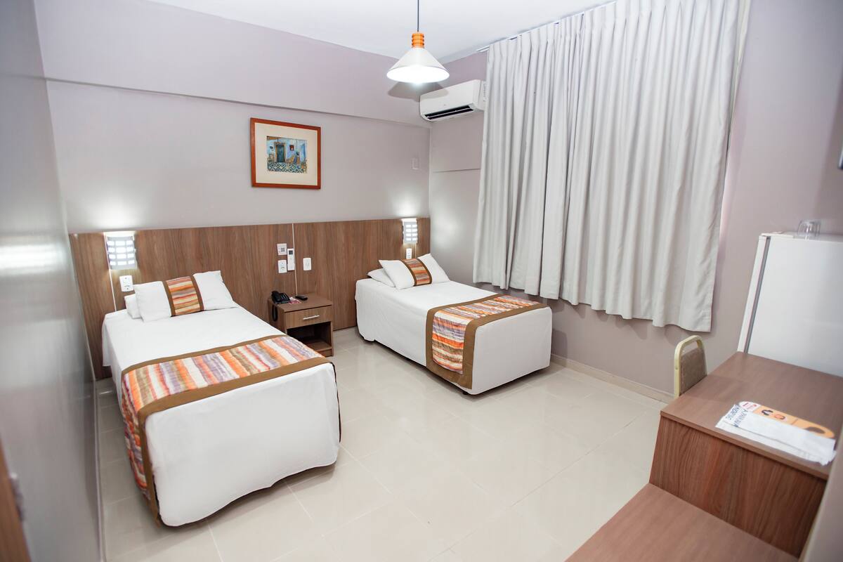 A hotel room with two beds, a desk, a chair, a nightstand, and a framed picture on the wall.