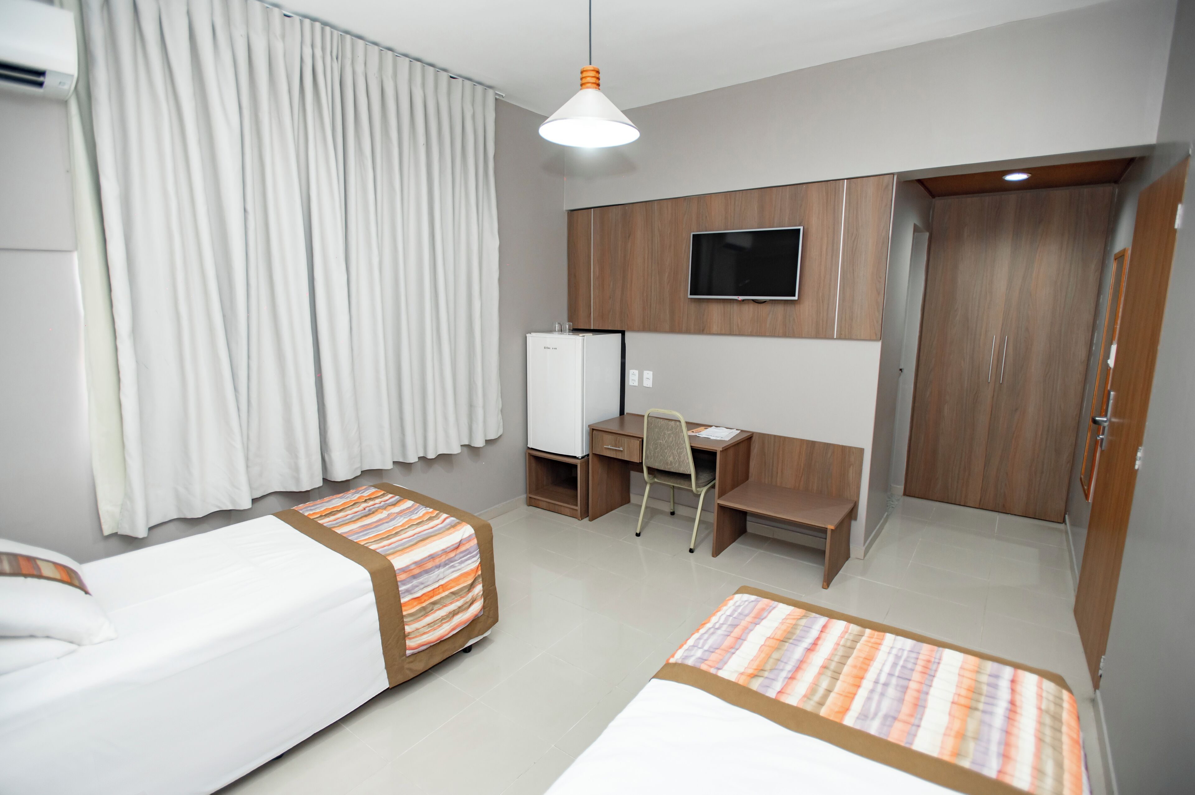 Hotellihuone, jossa on kaksi erillistä sänkyä, työpöytä tuolilla, televisio ja vaatekaappi.