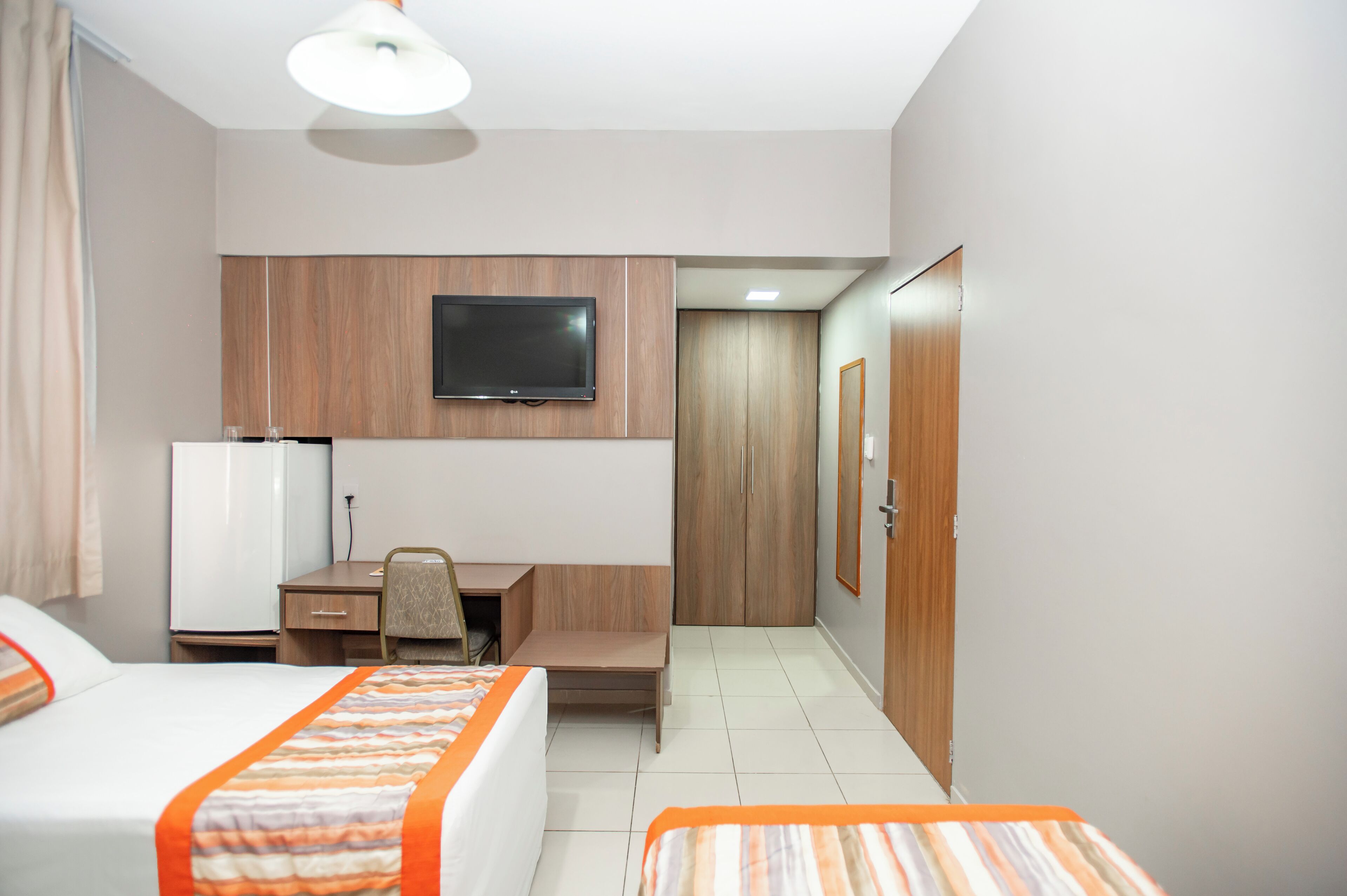 Een hotelkamer met twee bedden, een bureau, een stoel, een televisie en een kledingkast.