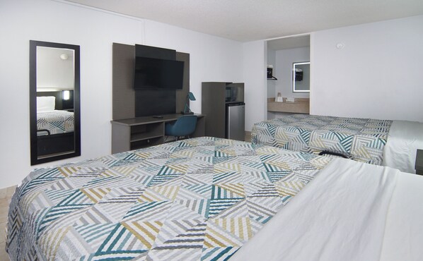 Une chambre d’hôtel équipée d’un lit, d’un bureau, d’une chaise, d’une télévision, d’un miroir et d’une petite kitchenette.