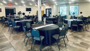 A conference room with multiple tables and chairs, a large pillar, a television, and a projector screen.