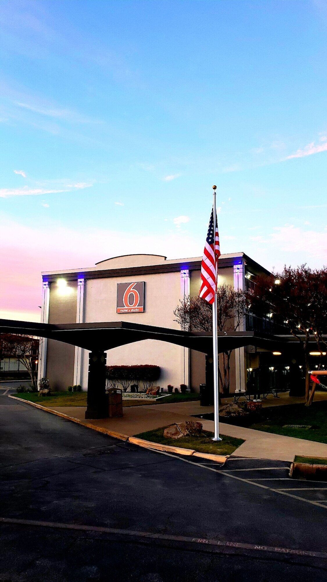 Un motel con un letrero con el número '6', una bandera estadounidense y un corredor cubierto.
