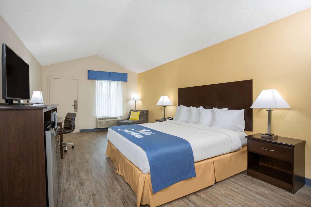 A hotel room with a bed, bedside lamps, a desk with a television, and a chair.