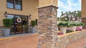 Un edificio de ladrillo con un pilar de piedra, plantas en macetas grandes y un adorno en la puerta.