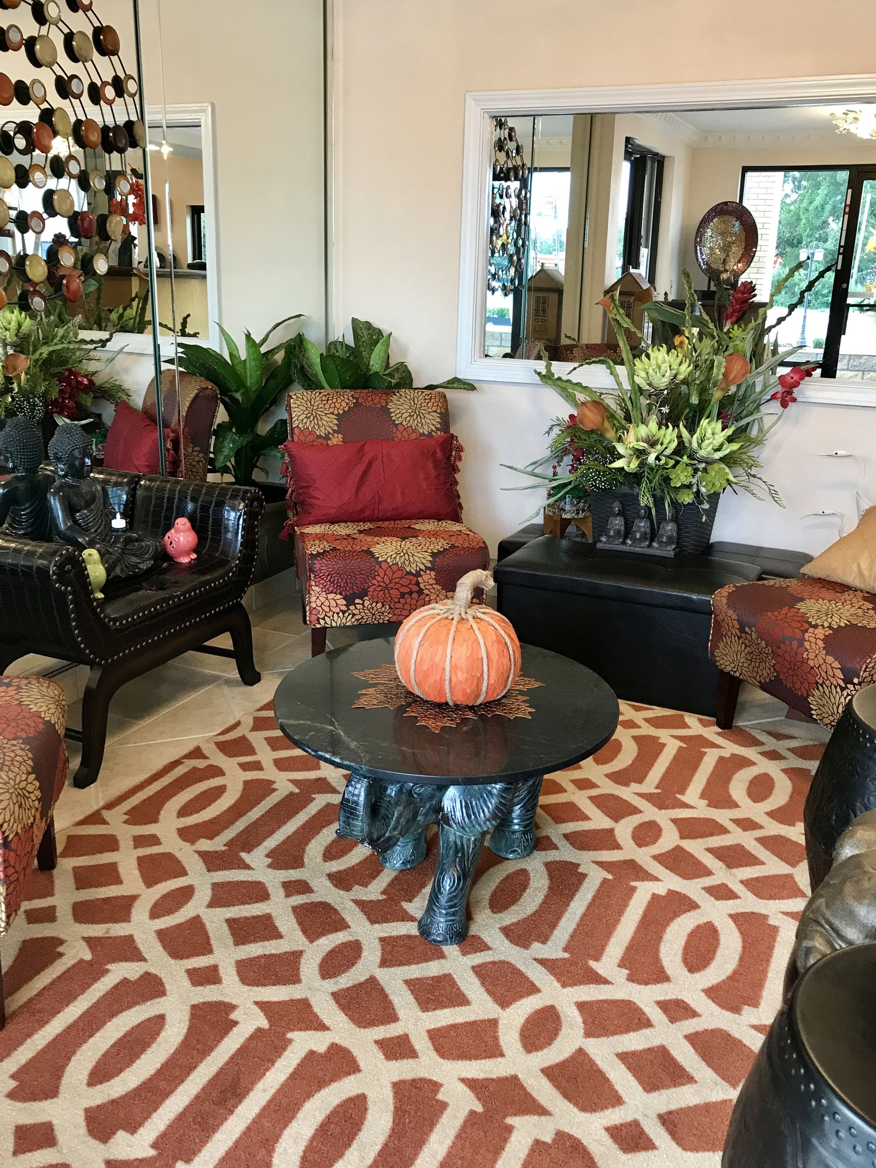 Uma sala de estar acolhedora com um tapete estampado, uma mesa redonda com um arranjo de abóboras e uma poltrona com estofamento floral.