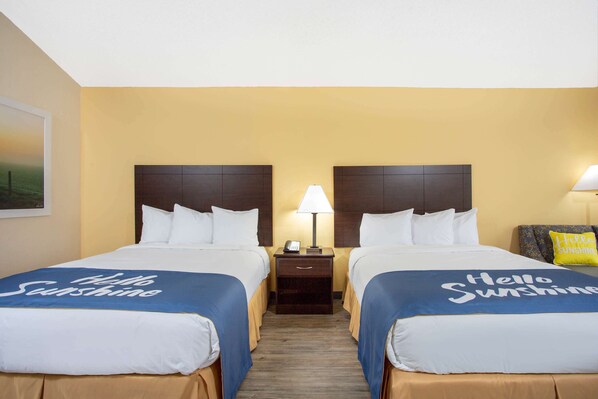A hotel room with two beds, each with a blue bedspread and white pillows. There is a nightstand with a lamp between the beds.