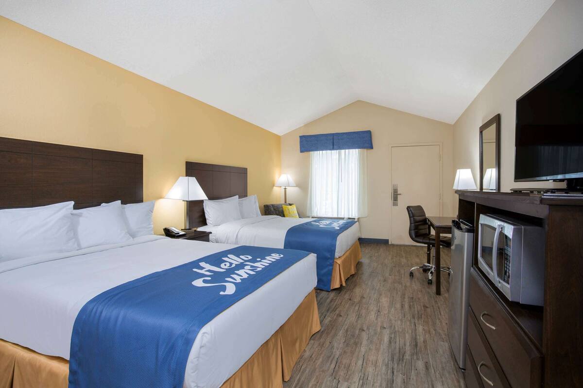 A hotel room with two beds, a desk, a chair, a TV, and a microwave.