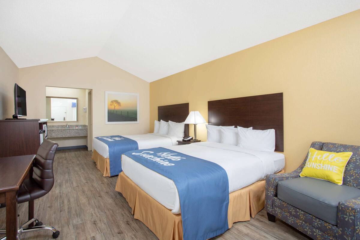 A hotel room with two beds, a desk, a chair, and a sofa.