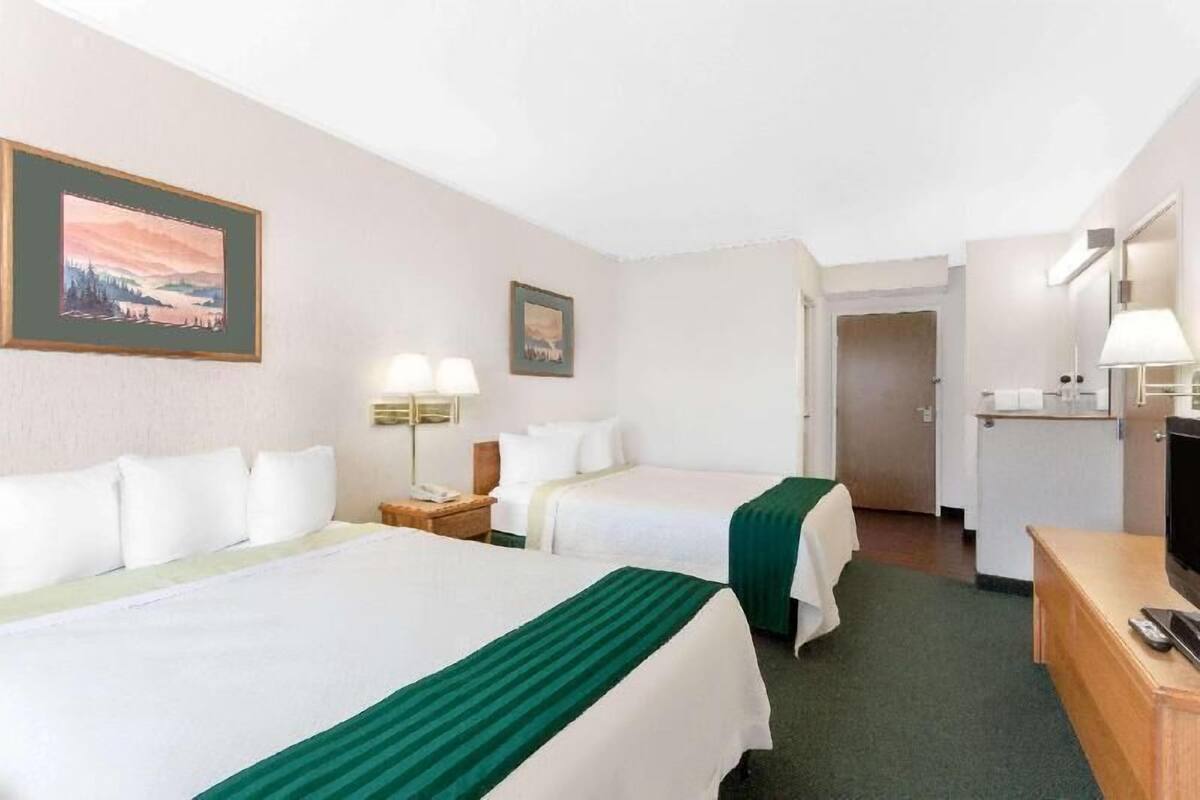 Une chambre d’hôtel avec deux lits, un bureau avec une télévision, une lampe et un tableau au mur.