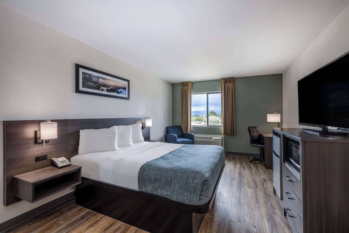 A hotel room with a large bed, bedside lamps, a desk with a TV, a chair, and a window with curtains.