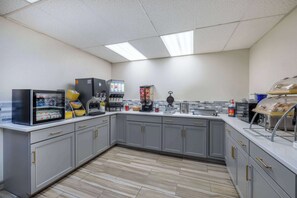 Une cuisine moderne avec des meubles gris, un four à micro-ondes, des machines à café et un présentoir à pain.