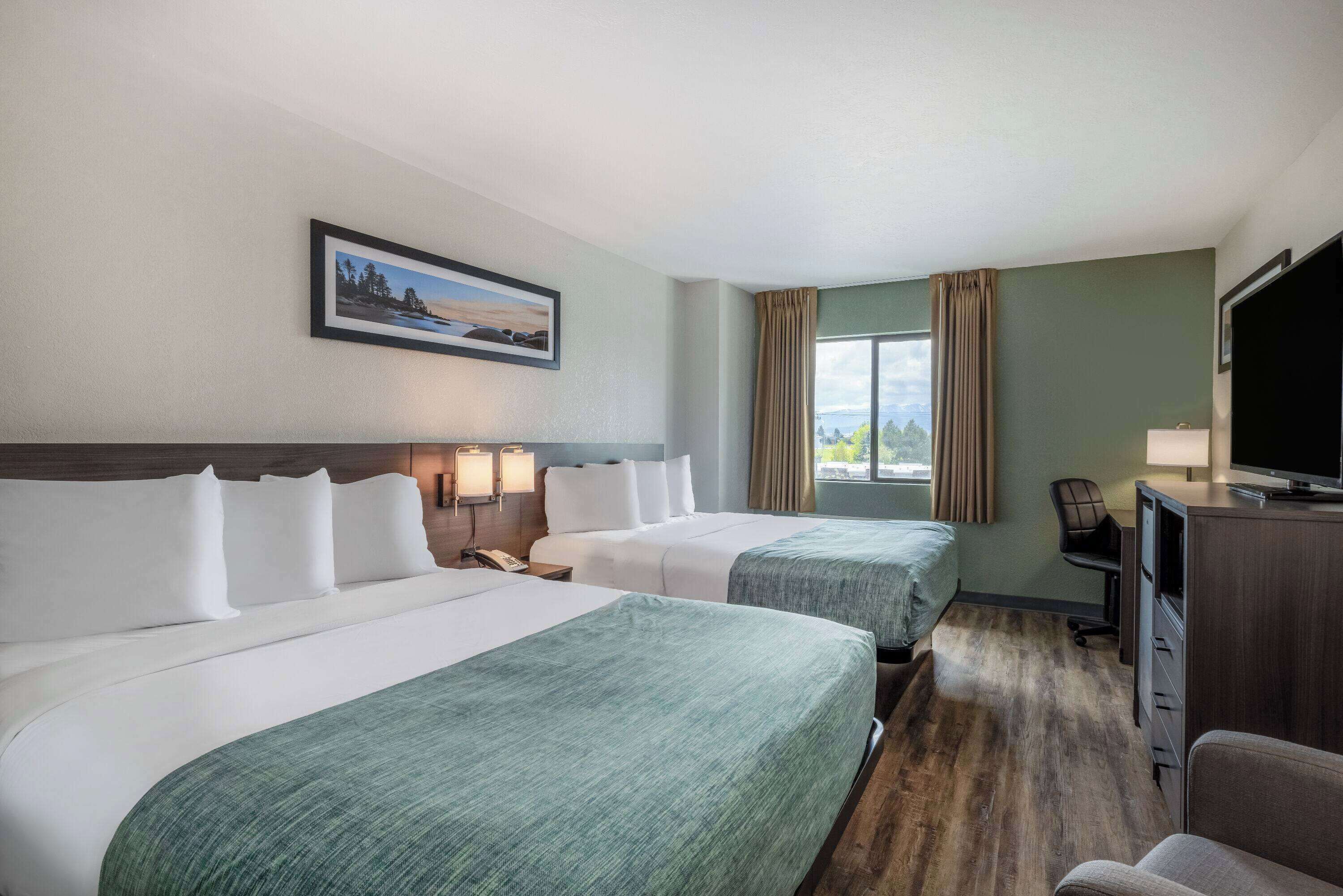 A hotel room with two beds, a desk with a TV, a chair, and a window with curtains.