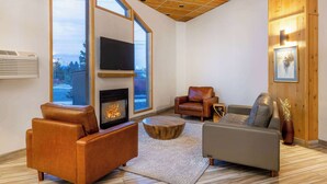 A modern living room with a fireplace, leather sofas, a coffee table, and a large window offering a view of the outdoors.