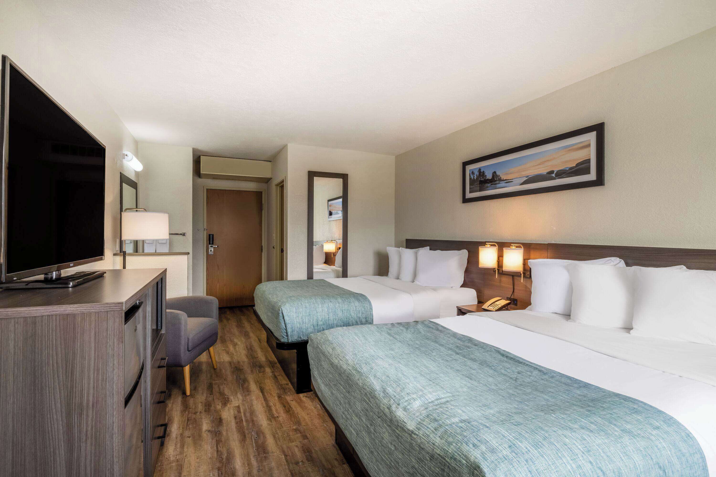 A hotel room with two beds, a desk with a TV, a chair, and a painting on the wall.
