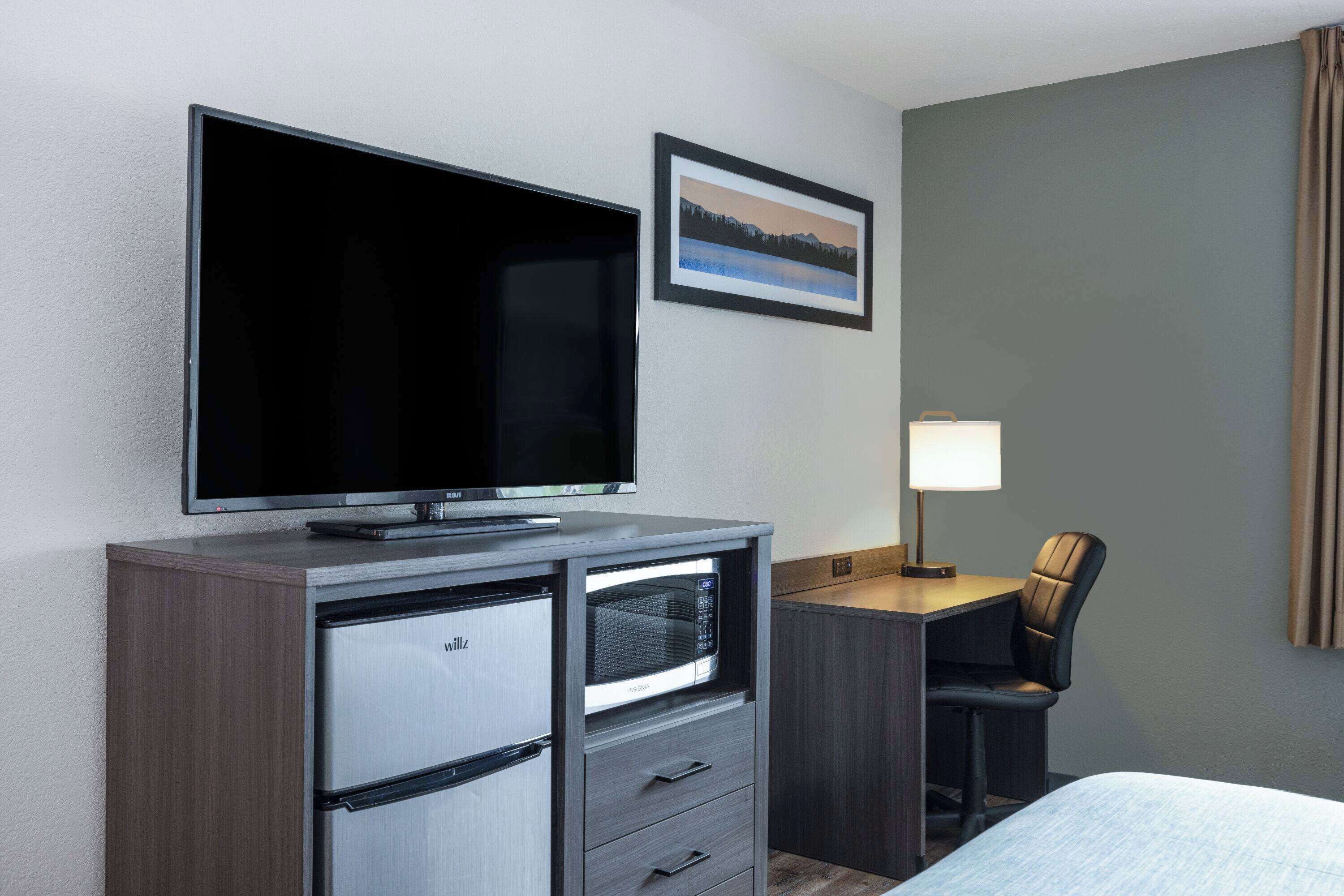 Een hotelkamer met een flatscreen televisie, een bureau met lamp, een stoel en een bed.