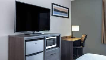 A hotel room with a flat-screen TV, a desk with a lamp, a chair, and a bed.