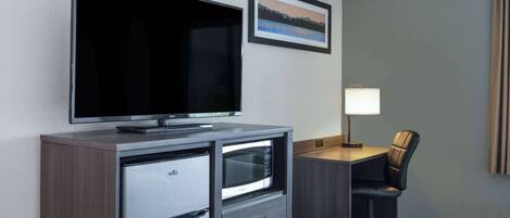 Een hotelkamer met een flatscreen televisie, een bureau met lamp, een stoel en een bed.