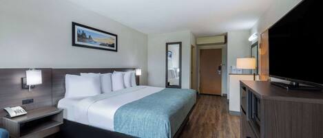 A hotel room with a bed, bedside table with a lamp, a TV, and a mirror.