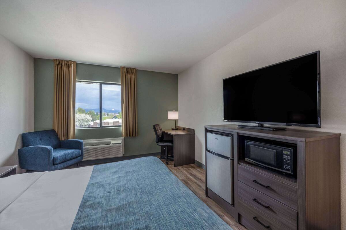 Une chambre d’hôtel équipée d’un lit, d’un bureau, d’une chaise, d’une télévision, d’un four à micro-ondes et d’une fenêtre avec des rideaux.