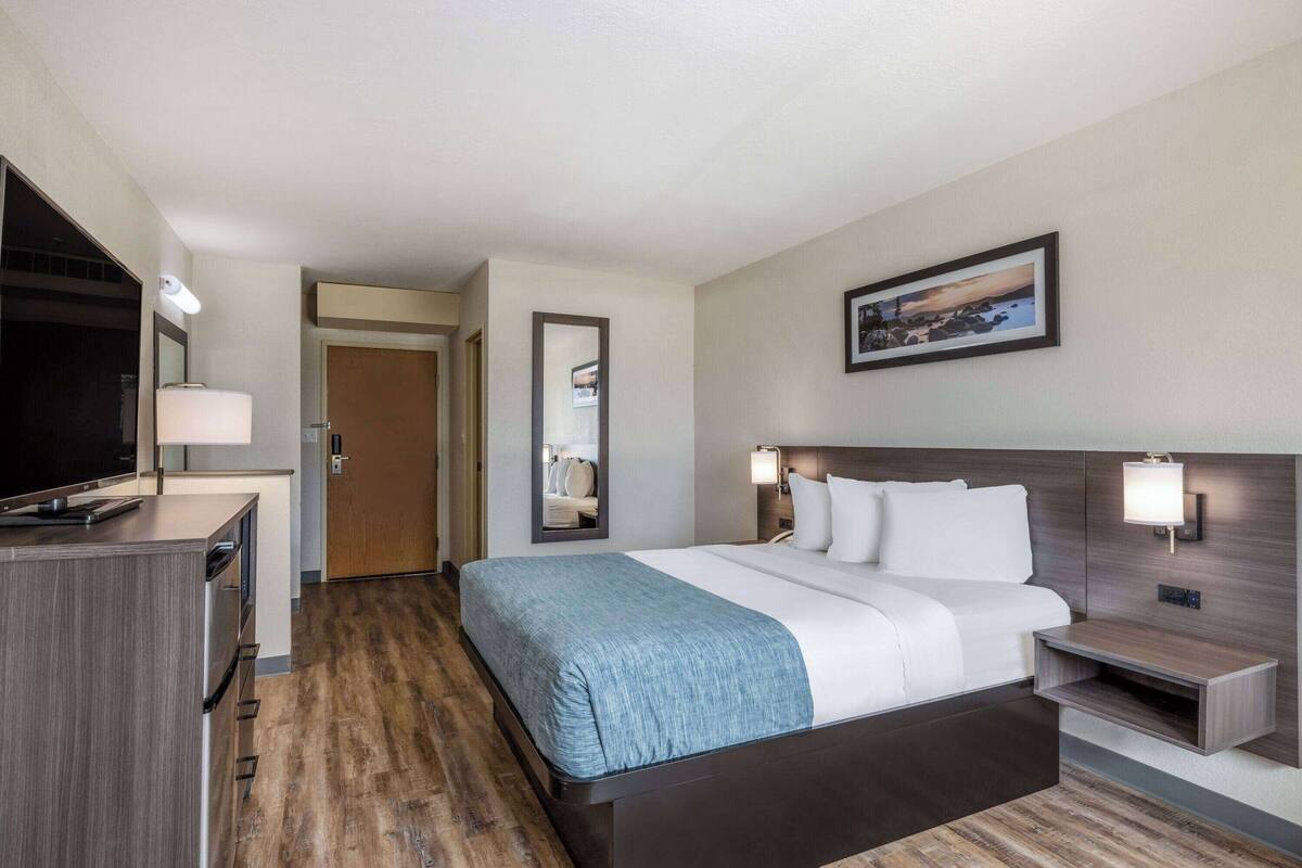 A hotel room with a bed, bedside tables, a TV, a desk, and a mirror.